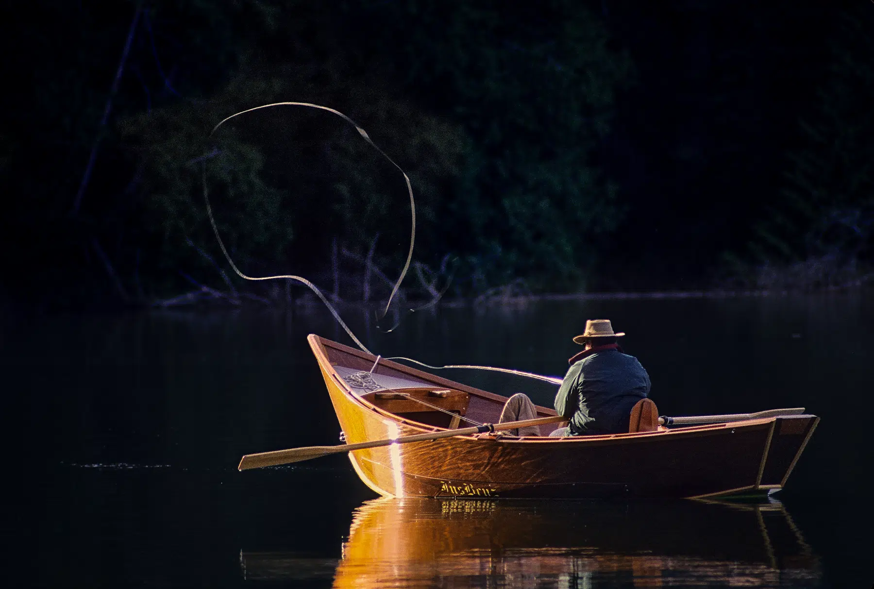 Man fly fishing from wooden boat on lake.