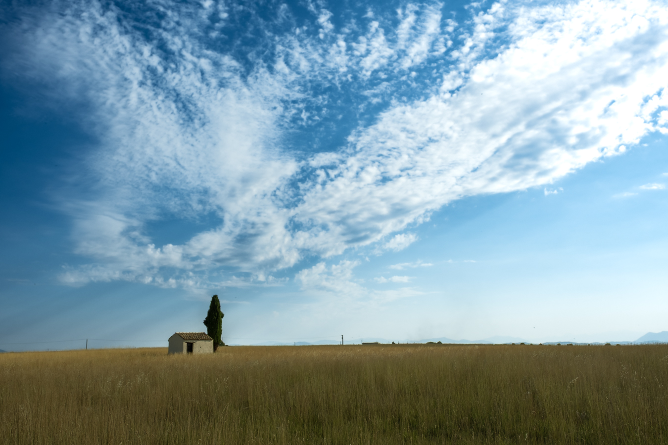 Rural landscape with house, cypress, and blue sky.